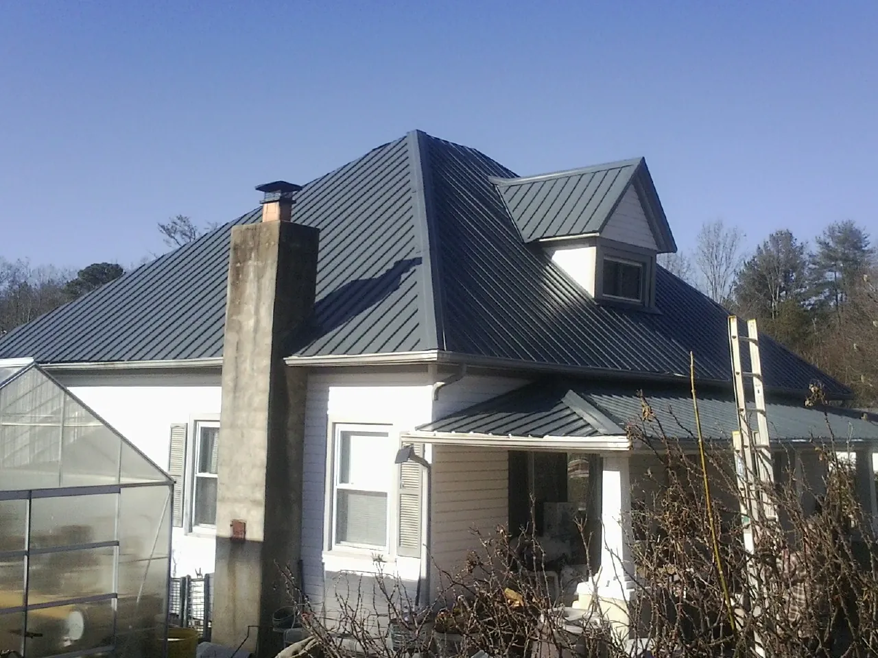 Dark blue standing seam metal roof on a white farmhouse with dormer — Slate & Tile Roof Repair by Roofing Brothers in North Olmsted