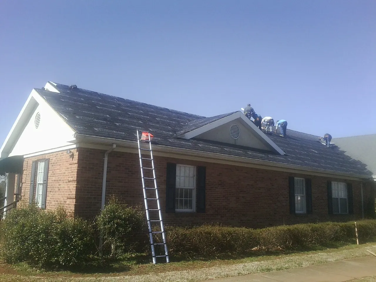 Crew tearing shingles off a brick ranch roof with a ladder set — Emergency Roof Repair work by our crew in North Olmsted