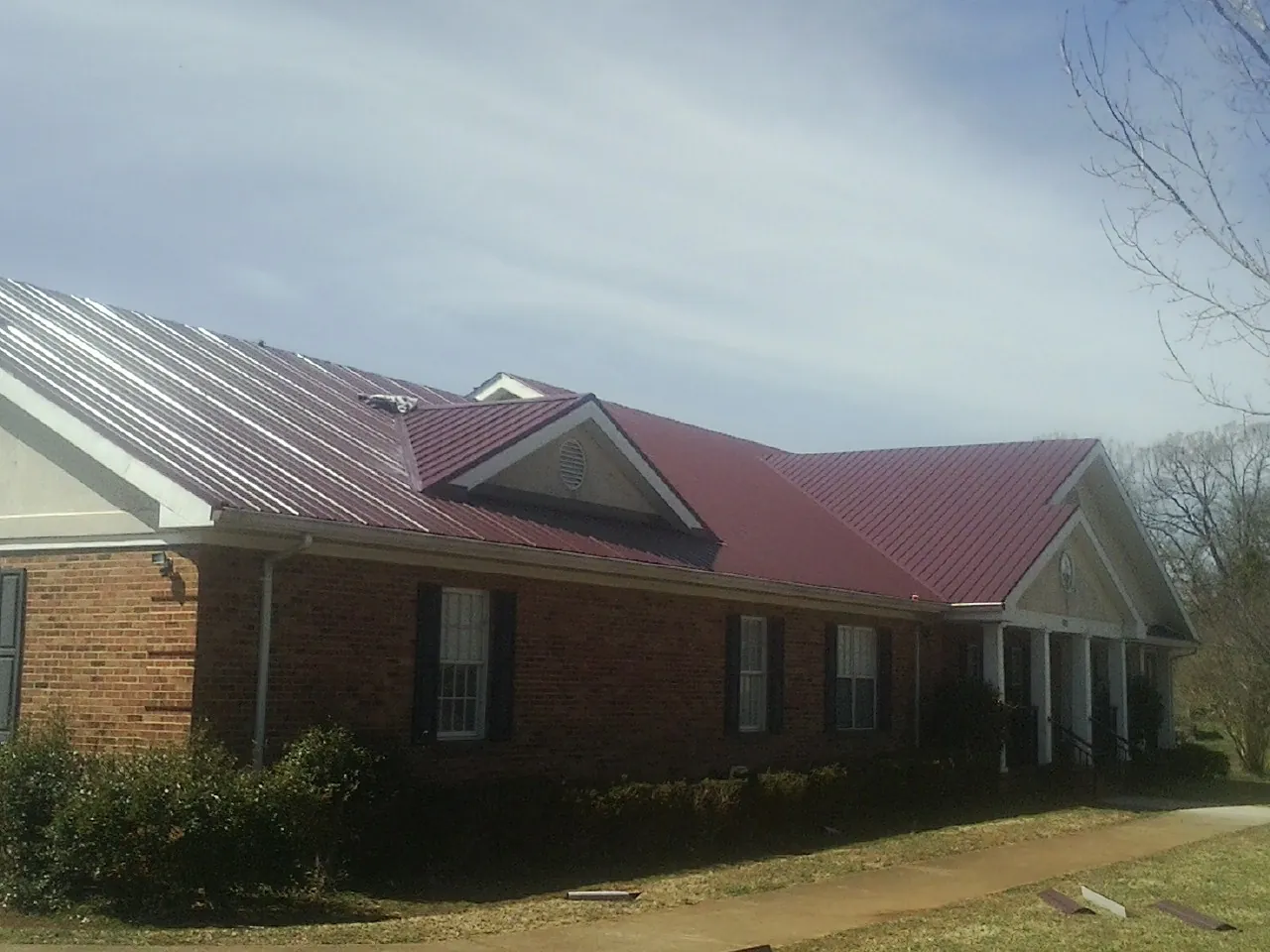 Red metal roof with gabled entries on a long brick building, from a Hail Damage Roof Repair job in North Olmsted