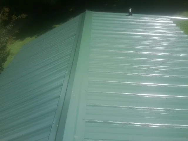 New green metal panels meeting at the ridge of a roof — Flat Roof Repair work by our crew in North Olmsted
