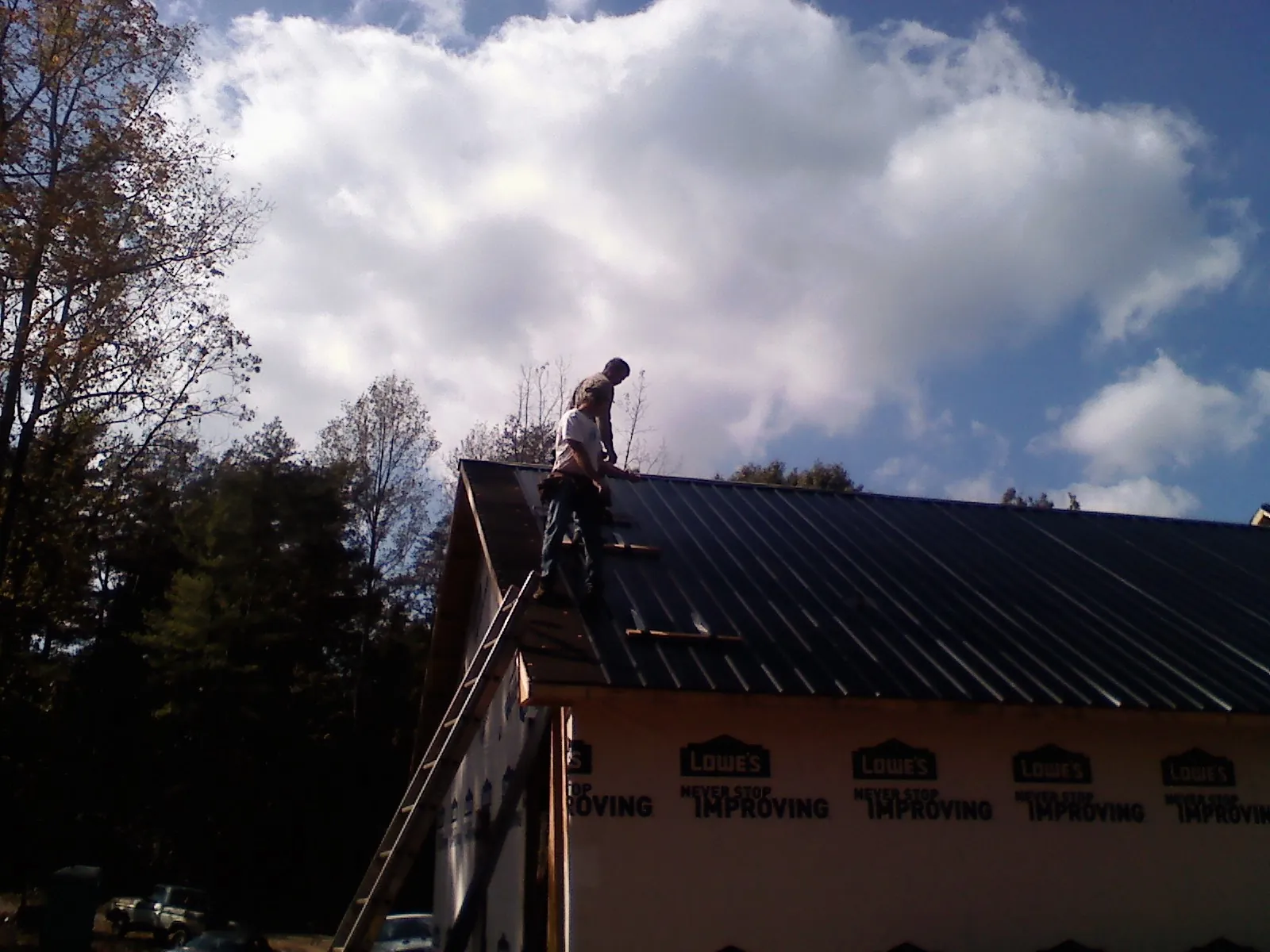 Roofer fastening dark metal panels high against a cloudy sky, from a Roof Inspection job in North Olmsted
