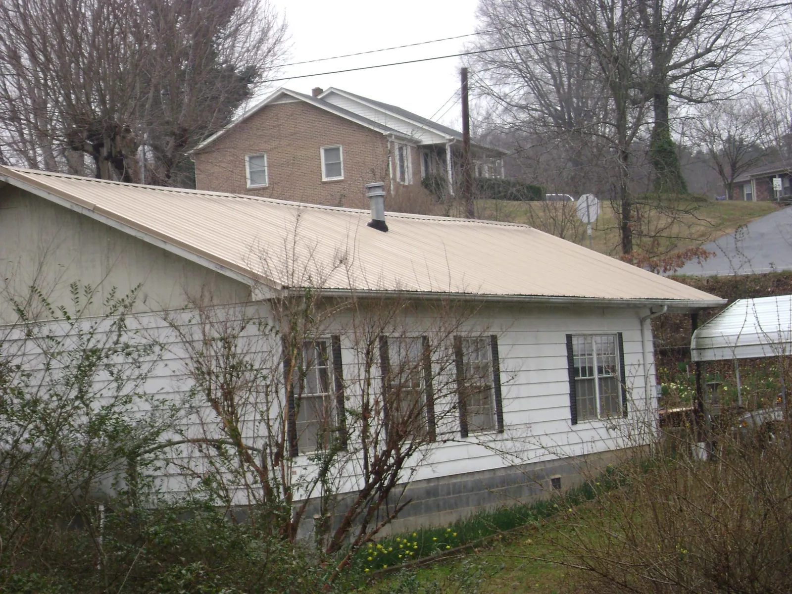 Tan metal roof on a white sided house set into a hillside — Commercial Roofing by Roofing Brothers in North Olmsted